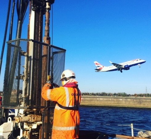 Site operative carrying out over water work as a plane fly's by in the background