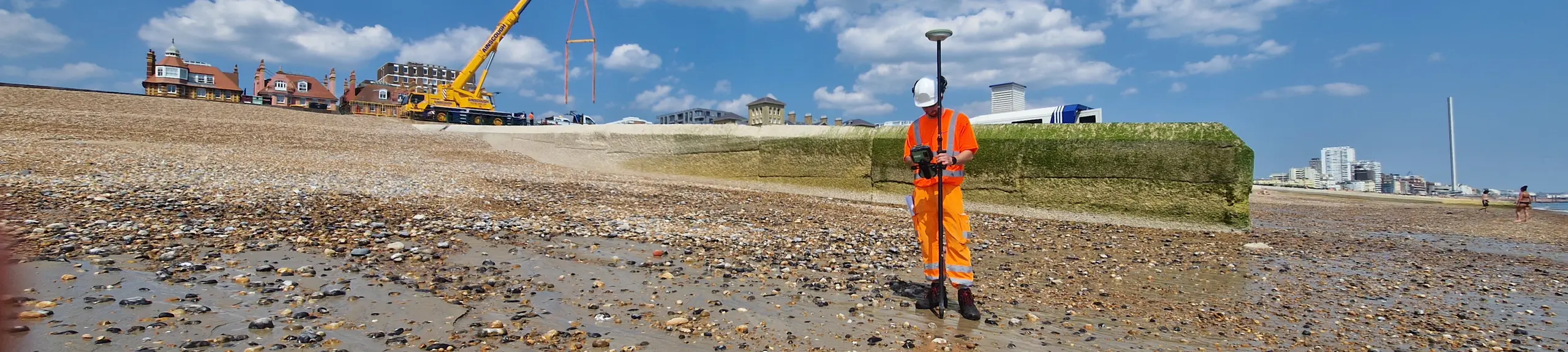 Site operative on Brighton Beach using a GPS for borehole location surveying with a Crain in the background 